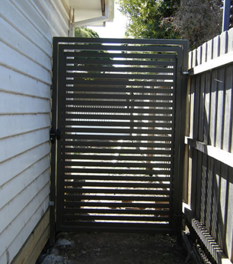 Slatted metal side gate installed between house wall and fence for secure backyard access in Melbourne.