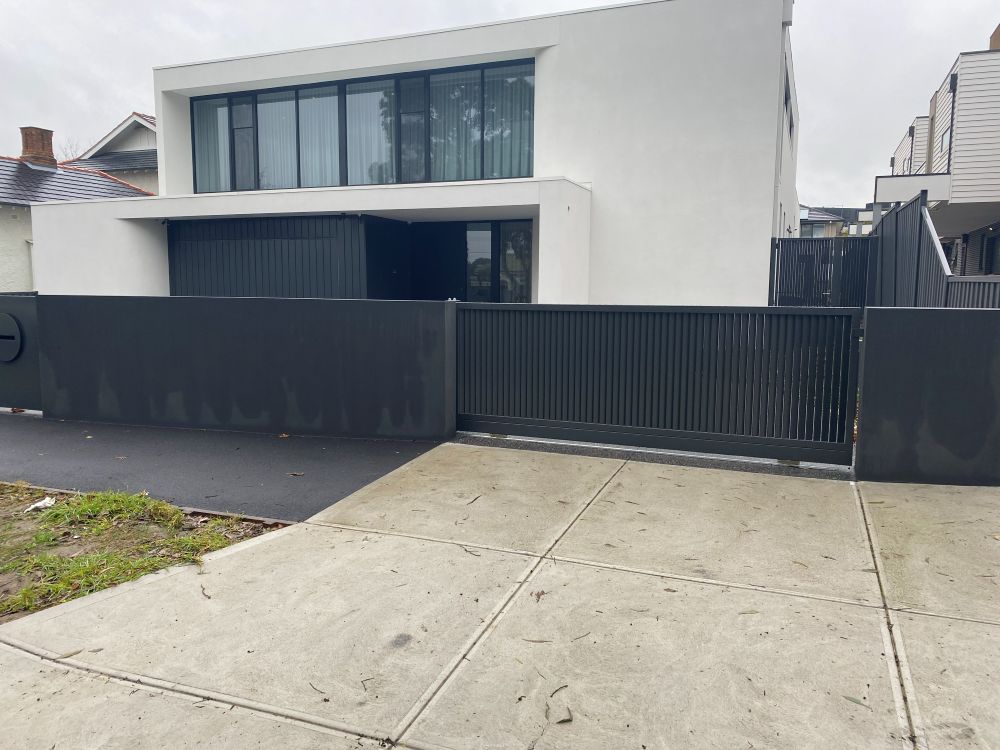 A modern two-story house with a black slatted fence and driveway gate