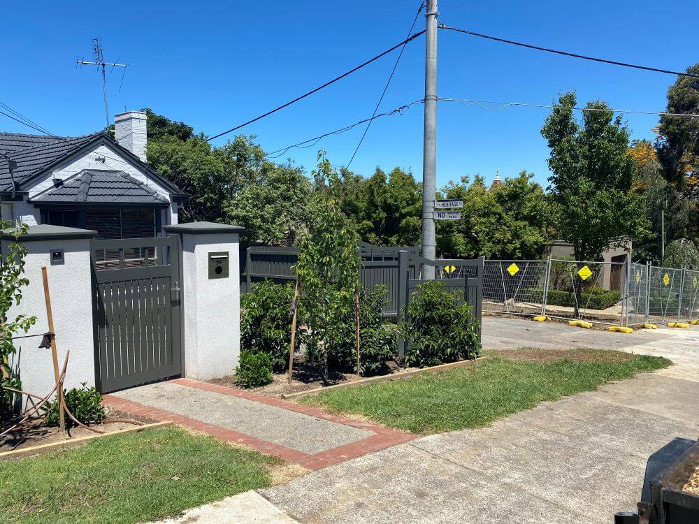 Full front frontage view showing matching aluminium pedestrian gate, driveway double gates, and rendered pillars in Ivanhoe.